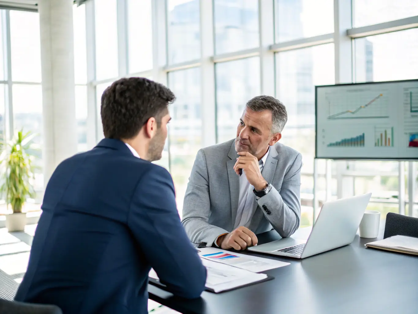 A professional executive in a suit, sitting at a large conference table, deeply engaged in a one-on-one discussion with a marketing consultant, surrounded by strategic documents and data visualizations, in a brightly lit modern office setting.